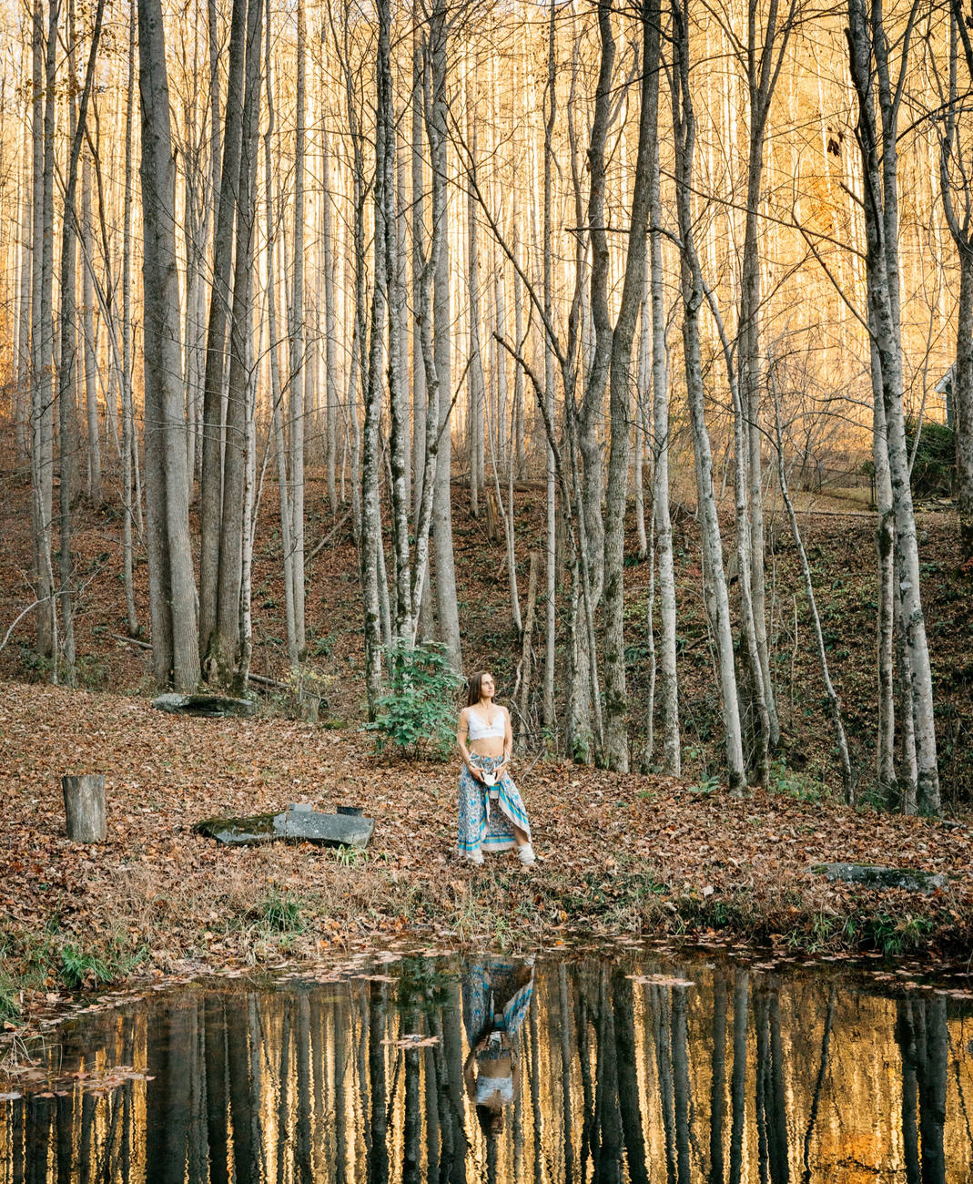 Raphaela in a white top among autumn trees beside a still forest pool